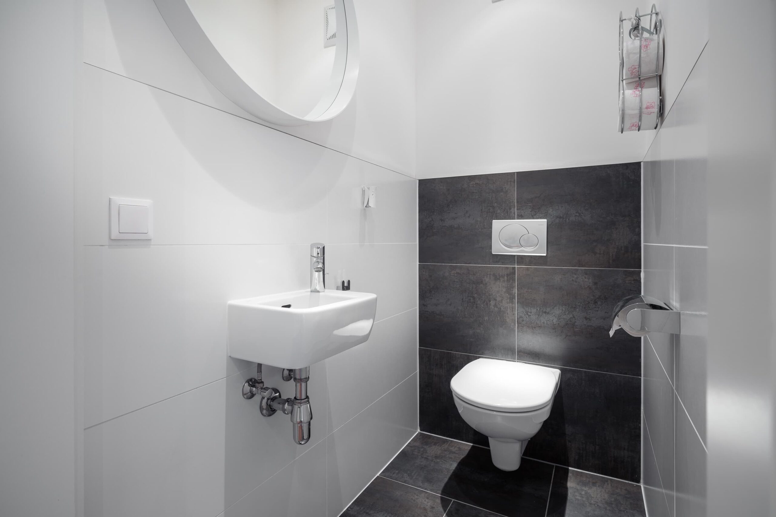 Modernes Gäste-WC mit Waschbecken, Spiegel und eleganten Fliesen im CityFLAT 38 Appartement by globboard in Schladming-Dachstein.