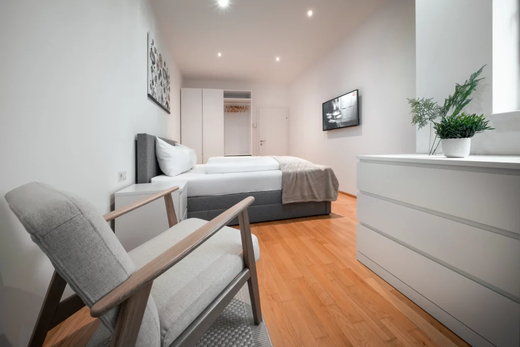 Stilvolles Schlafzimmer im CityFLAT 38 Appartement by globboard in Schladming-Dachstein, mit gemütlichem Doppelbett, Sessel, Kommode, Schrank und Fernseher.