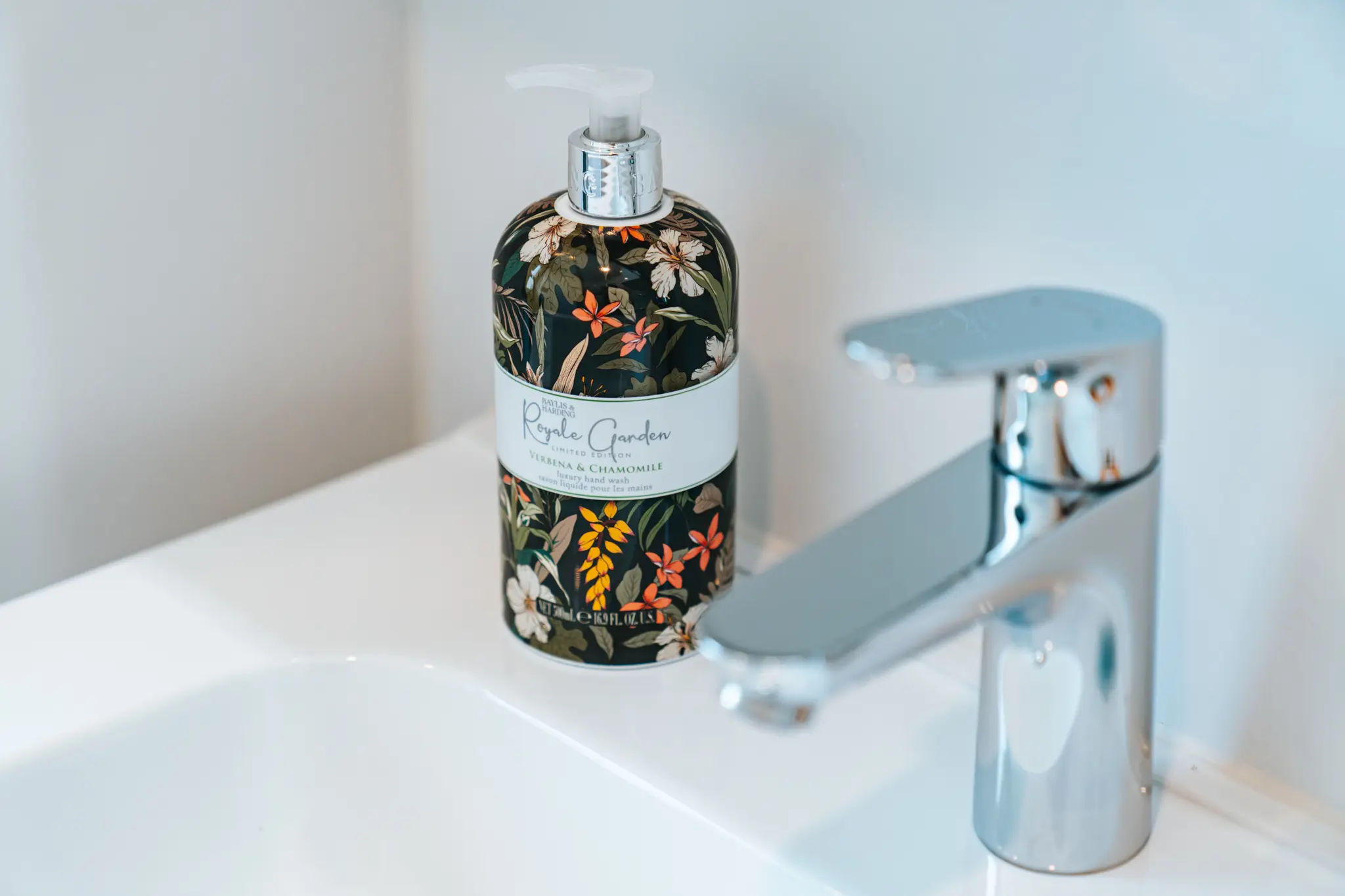 Nahaufnahme eines eleganten Waschbeckens mit einem modernen Wasserhahn aus glänzendem Chrom und einer stilvollen Handseife in einer floral verzierten Verpackung.