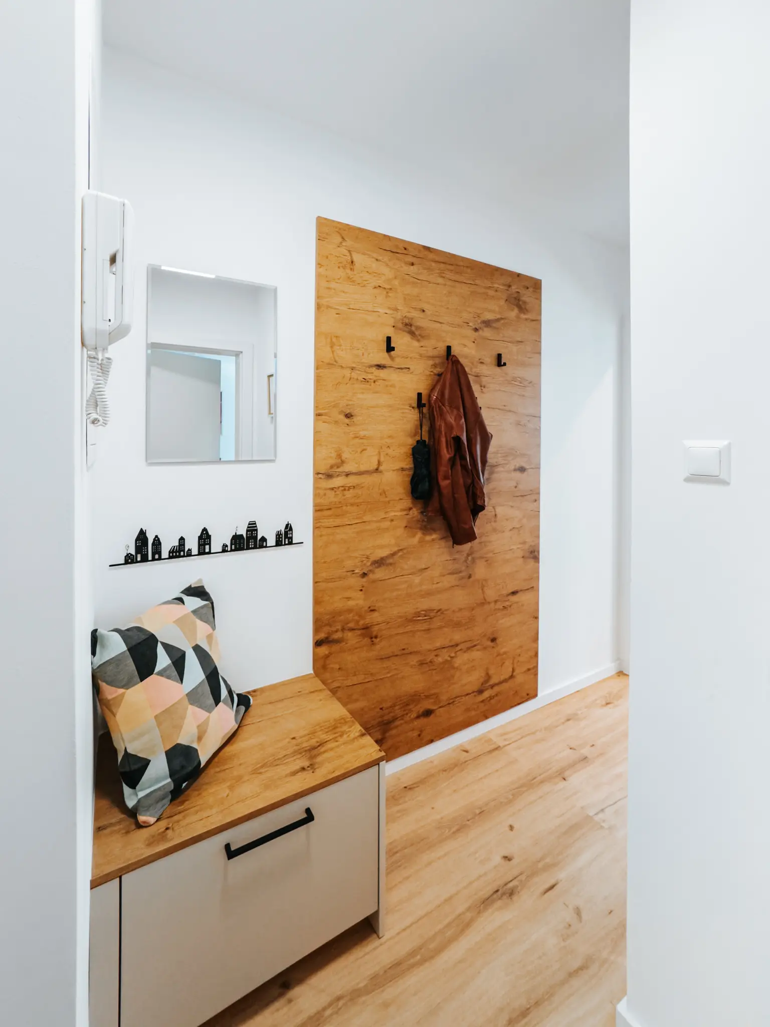 Ein einladender Eingangsbereich im Appartement Grand Prix in Zeltweg mit einer stilvollen Holzwand mit Kleiderhaken, einer Sitzbank mit farbenfrohem Kissen und einer dekorativen Ablage.