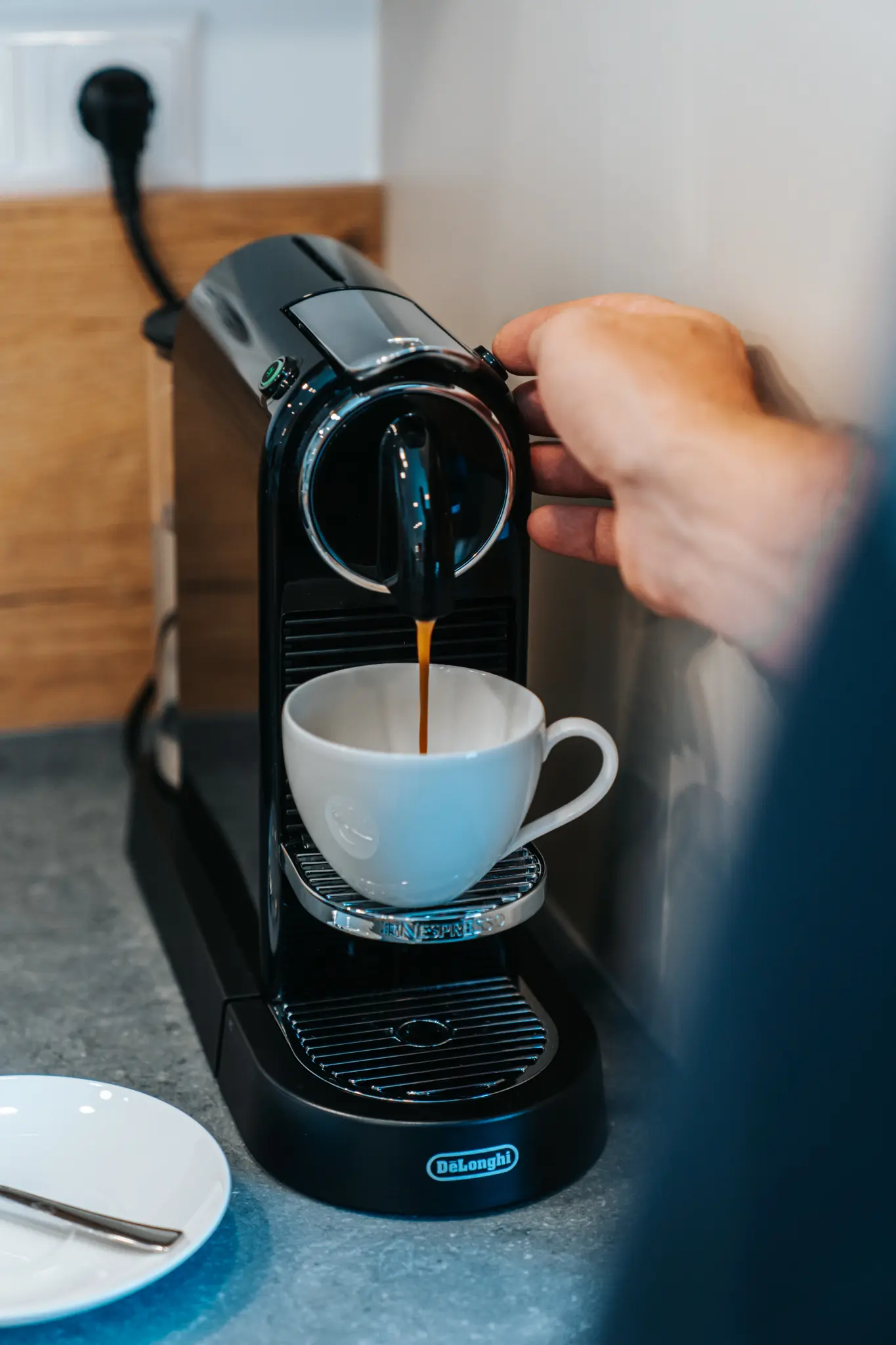 Eine De'Longhi Nespresso-Kaffeemaschine, die gerade einen frischen Espresso in eine weiße Tasse brüht, gehalten von einer Hand.