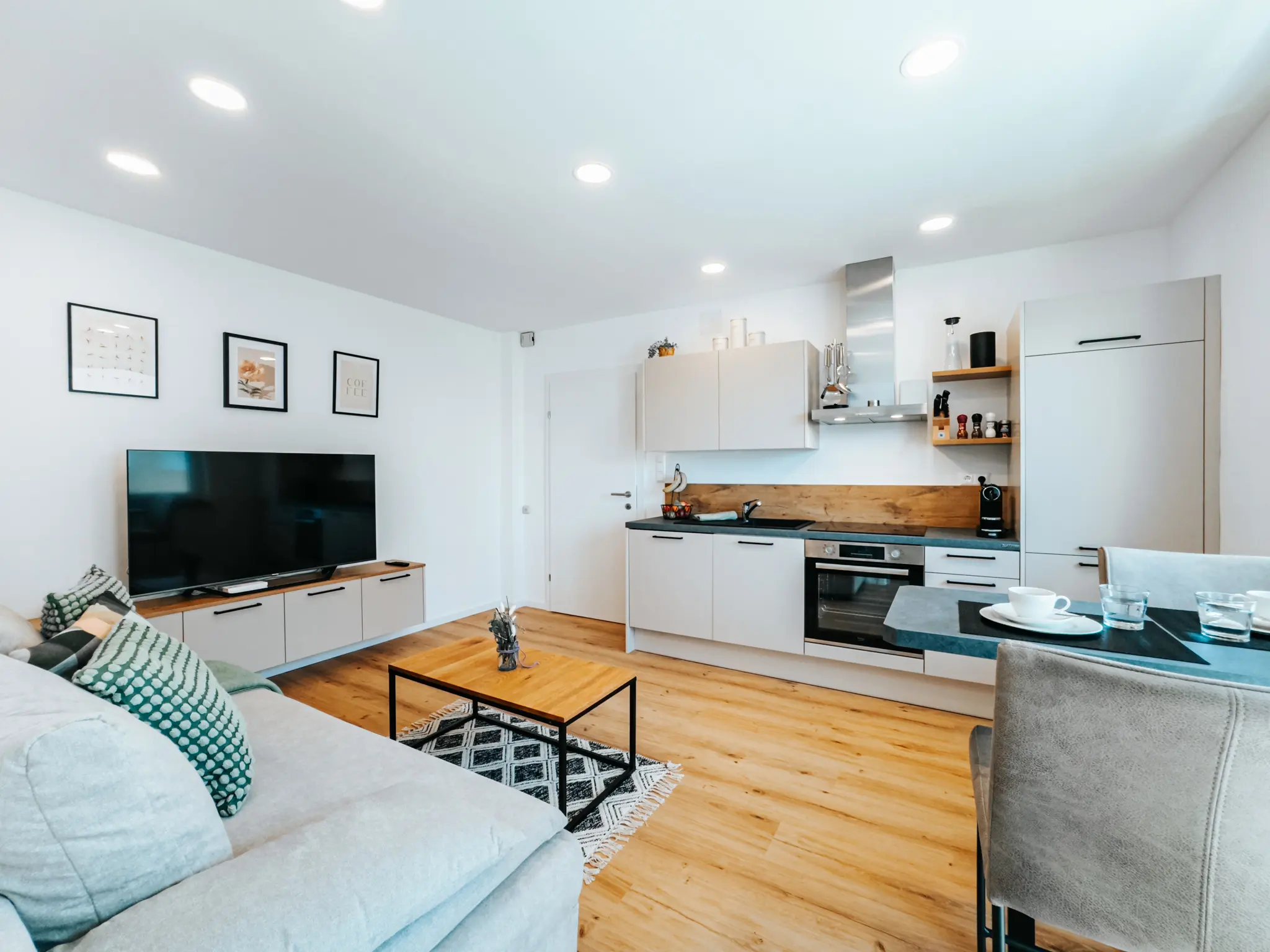 Das moderne Wohnzimmer und die Küche im Appartement Grand Prix in Zeltweg. Der offene Wohnbereich umfasst eine gemütliche Couch, einen großen Flachbildfernseher und eine voll ausgestattete Küchenzeile mit Essbereich.