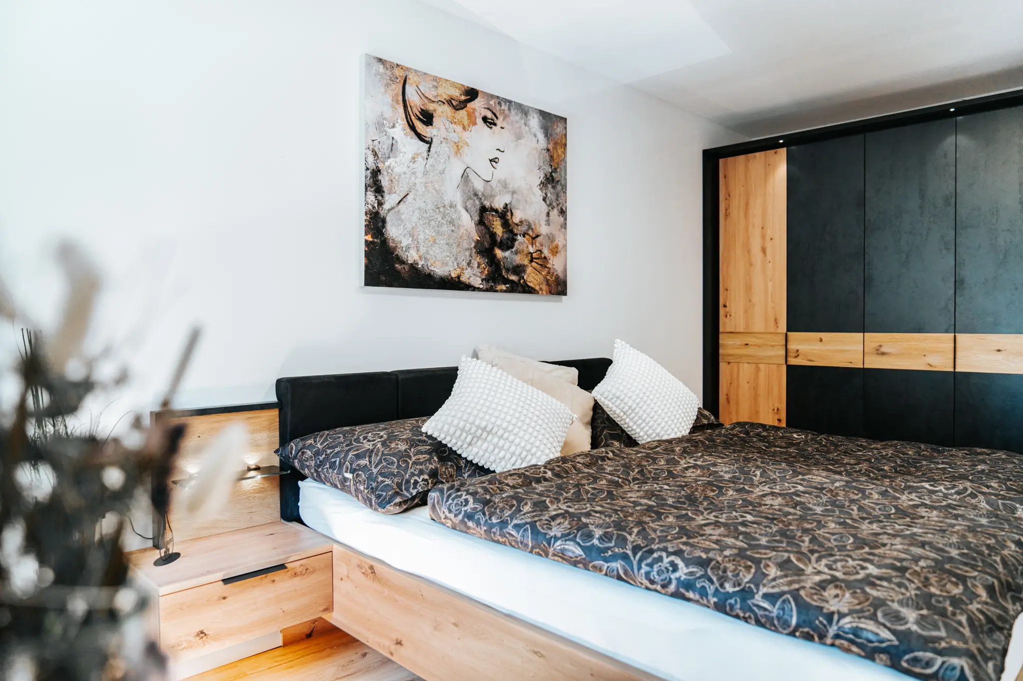 Helles und modernes Schlafzimmer im Appartement Grand Prix in Zeltweg mit einem großzügigen Doppelbett, stilvollem Wandbild und einem großen Einbauschrank in Holz- und Schwarzoptik.