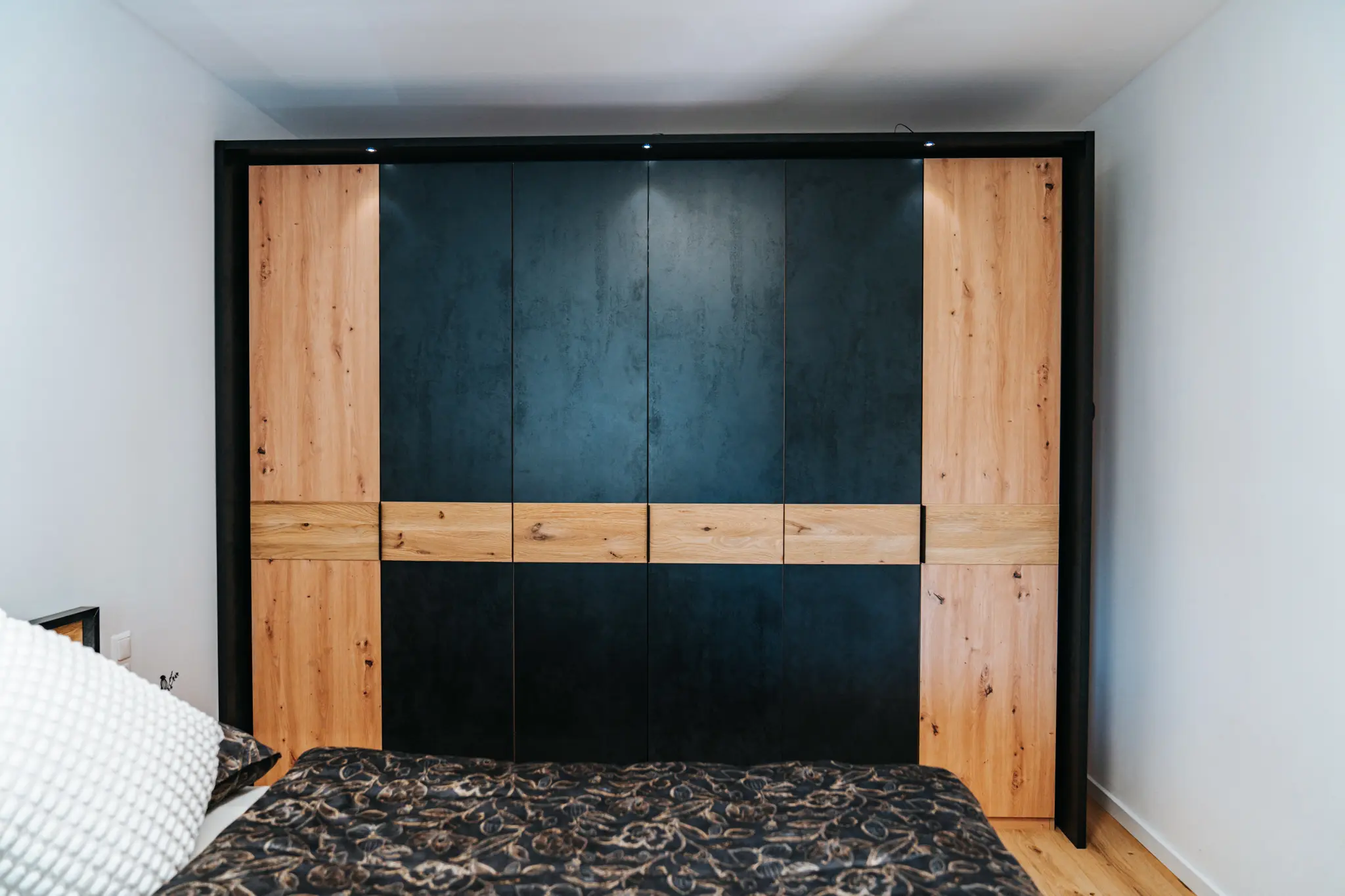 Ein moderner Kleiderschrank im luxuriösen Grand Prix Appartement in Zeltweg. Der Schrank kombiniert dunkle, glatte Oberflächen mit warmem Holzdekor und verfügt über klare Linien, die dem Raum eine elegante und zeitlose Atmosphäre verleihen.