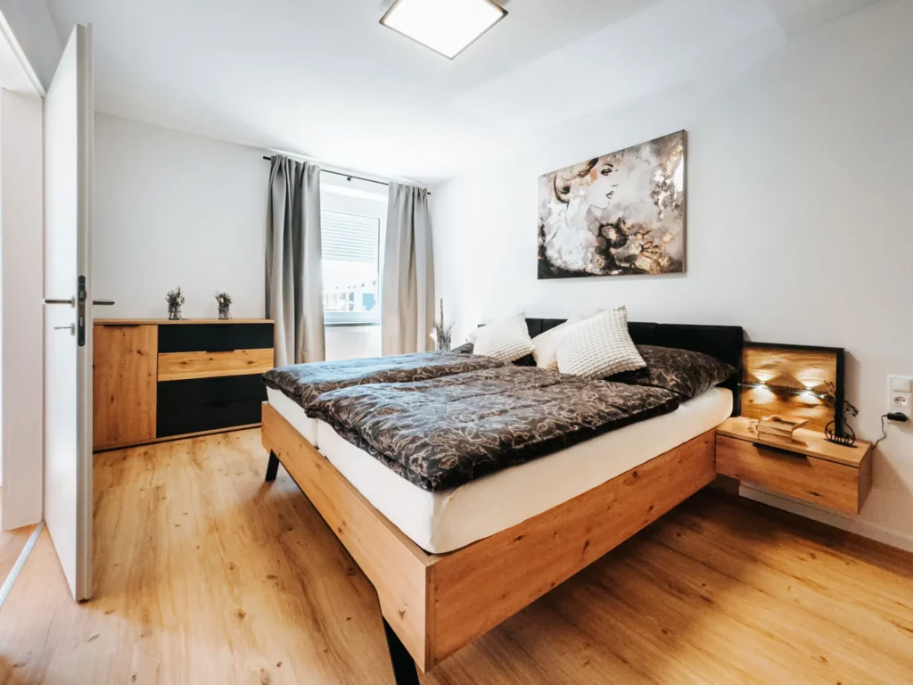 Ein luxuriös eingerichtetes Schlafzimmer in einem modernen Appartement in Zeltweg, nahe dem Red Bull Ring in Spielberg. Stilvolles Ambiente mit Holzmöbeln, gemütlichem Doppelbett und künstlerischer Wanddekoration.